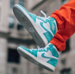 Teal and white high-top sneakers in mid-air against a blurred urban backdrop, orange pants visible at the edges.