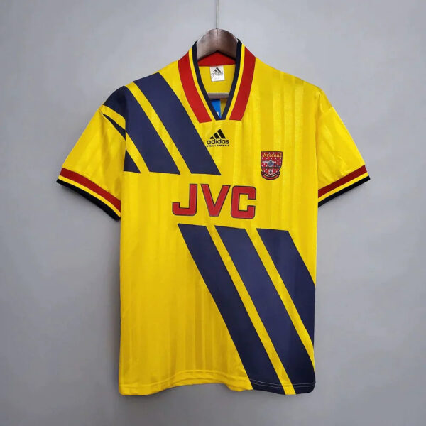 Yellow Arsenal football jersey with blue diagonal stripes and JVC sponsor on the front, Adidas badge above the crest, short sleeves with red-black-yellow trim, hanging on a hanger.