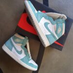 Turquoise and white Air Jordan 1 sneakers resting on a black Nike box with a red swoosh.