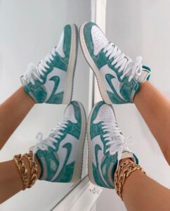 Teal and white sneakers pressed together in a mirrored pose, with gold chain bracelets on both wrists visible at the sides.