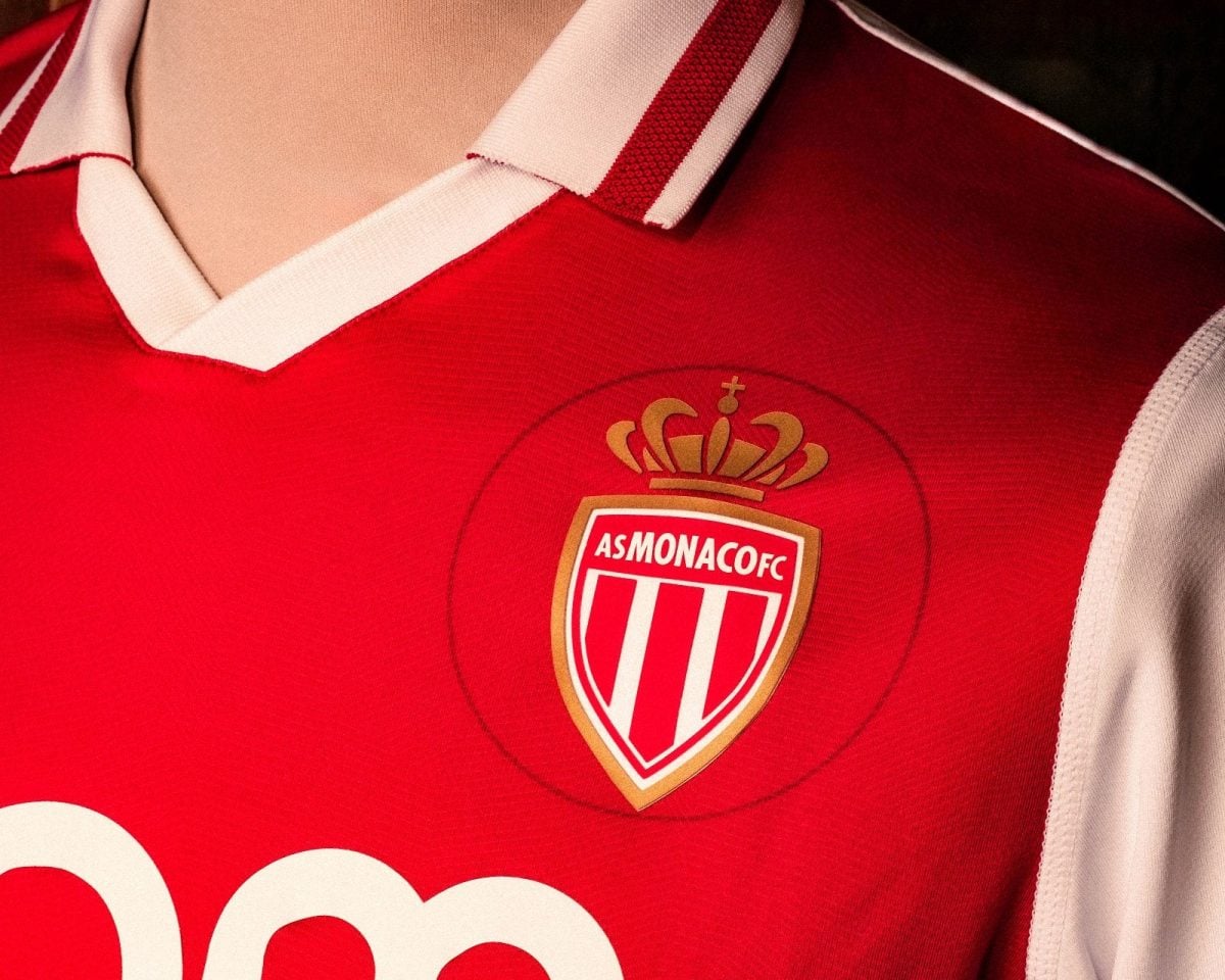 Close-up of a red AS Monaco football jersey featuring the crest with a gold crown and white-red shield prominently on the chest area.