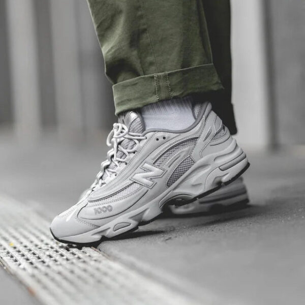 Close-up of a gray athletic sneaker stepping on a curb, with olive-green rolled pants visible above the shoe.