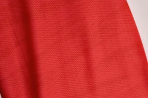 Close-up of red fabric with a fine textured weave and soft folds along the left edge.",