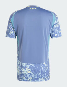 Back view of a blue athletic shirt with a solid blue back panel and teal side panels, water-splash pattern on sleeves and hem, three yellow X marks on the collar area.