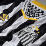 Close-up of a black-and-white striped soccer jersey with a yellow trim, Umbro logo, and a crest featuring a crown and stars.