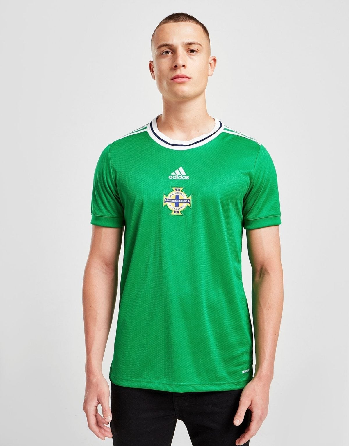 Portrait of a young man wearing a green Northern Ireland football jersey, facing the camera against a light gray background.