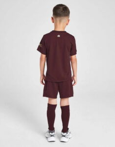 Child wearing a maroon soccer kit viewed from the back: short-sleeve shirt, shorts, long maroon socks, and white sneakers.