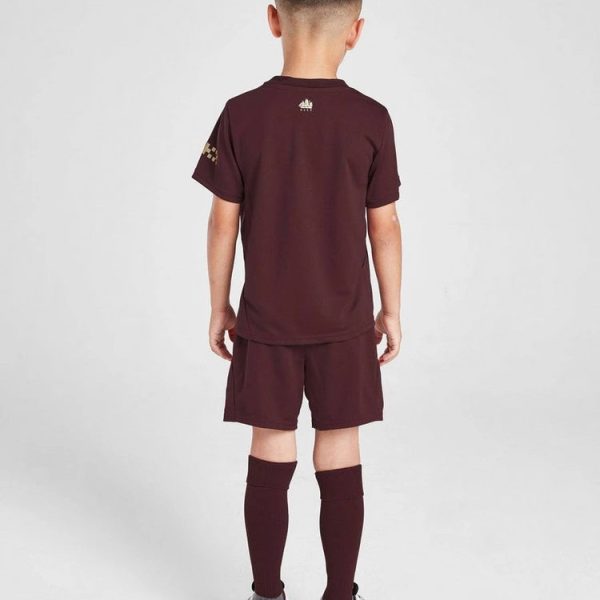 Child wearing a maroon soccer kit viewed from the back: short-sleeve shirt, shorts, long maroon socks, and white sneakers.