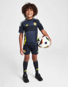 Smiling boy in a navy Scotland football kit holding a soccer ball, standing against a light background.