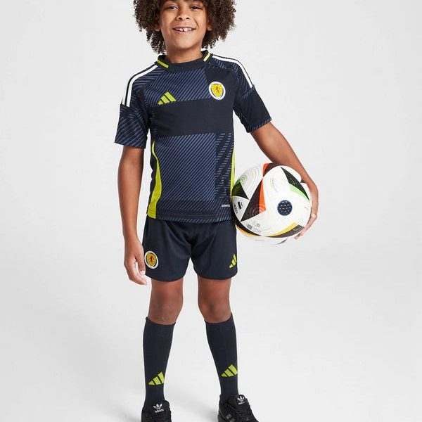 Smiling boy in a navy Scotland football kit holding a soccer ball, standing against a light background.