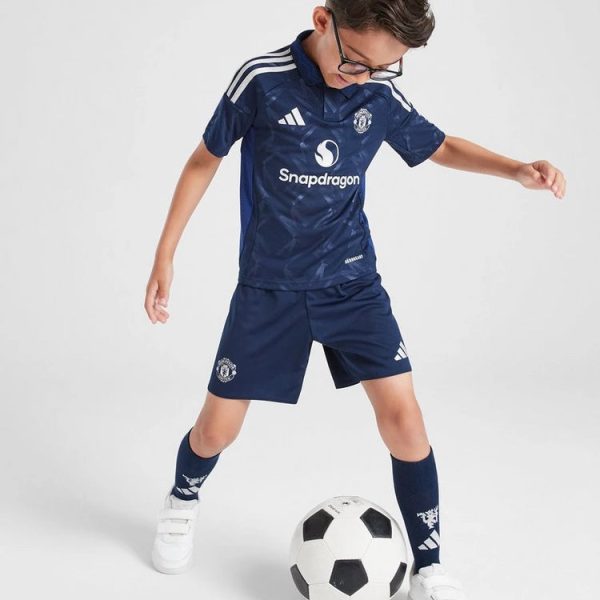 Young boy in a navy Manchester United soccer kit with Snapdragon sponsor, kicking a soccer ball on a white background.