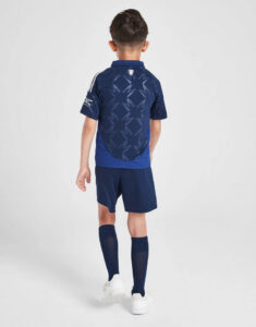 Back view of a child in a navy soccer kit with a patterned back panel, blue shorts and socks, and white shoes.