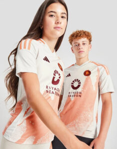 Two young models wearing matching white and peach Riyadh Season jerseys, posing together with logos visible on the shirts.