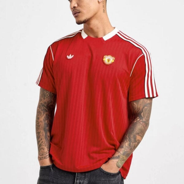 Man wearing a red Manchester United jersey with white sleeve stripes, standing with hands in pockets.