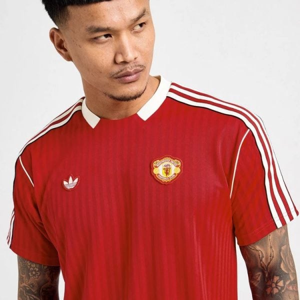 Man wearing a red Manchester United football jersey with white stripes on the sleeves, looking to the right.