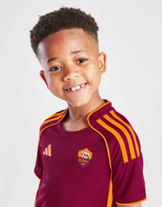 Smiling young boy in a maroon Roma soccer jersey with orange trim and logo visible, facing camera.