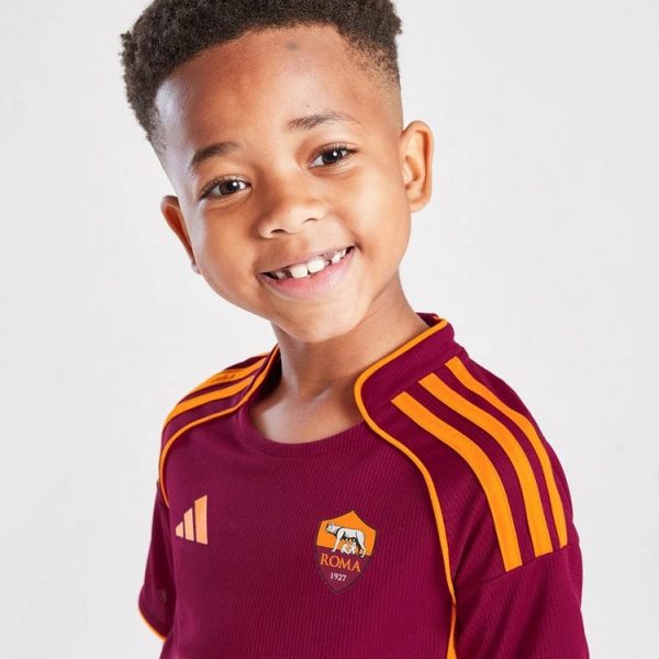 Smiling young boy in a maroon Roma soccer jersey with orange trim and logo visible, facing camera.