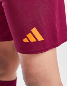 Close-up of maroon athletic shorts with an orange Adidas logo near the hem.