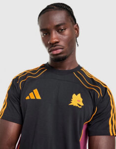 Portrait of a man with braids wearing a black athletic shirt with orange stripes and a yellow wolf logo on the chest.