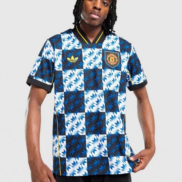Person wearing a blue and white geometric Manchester United football jersey with Adidas logo and crest, standing against a light gray backdrop.