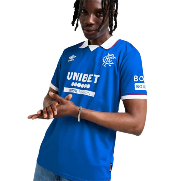 Athlete modeling a blue soccer jersey with sponsor logos, white collar, and red-trim sleeves.