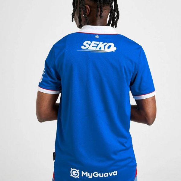 Back view of a person wearing a blue polo jersey with white SEKO logo on the upper back and white trim at the collar and sleeves; jeans visible at the bottom. This is a team or sponsor jersey showing branding on the back: SEKO and MyGuava logos.