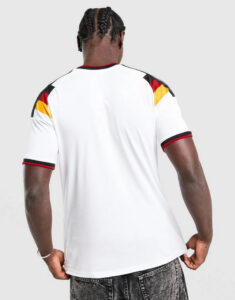Back view of a man wearing a white athletic t-shirt with black/red/yellow color blocks on the shoulders, paired with dark jeans.