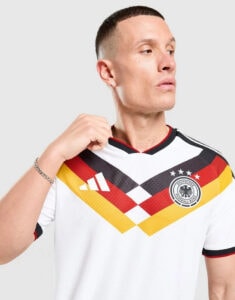 Man wearing a white Germany national football team jersey with black-red-gold chevrons, looking to the right while adjusting the collar.