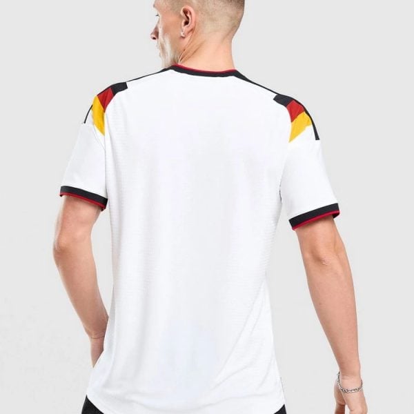 Back view of a man wearing a white football jersey with black, red, and yellow shoulder accents on the sleeves and collar edge.