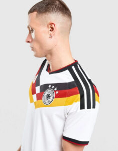 Side profile of a man in a white Germany national team jersey with black, red, and gold stripes and crest on the chest markups the Adidas design.
