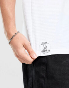 Close-up of a white Adidas jersey hem with a visible brand label and a metal bracelet on the wrist.