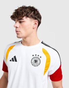 Side profile of a young man wearing a white Germany national football jersey with black logo, stars, and yellow accents on a light gray background