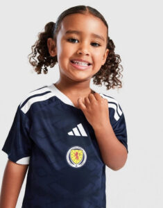 Smiling young girl wearing a dark blue Scotland football jersey with Adidas logo, holding the collar toward the camera.