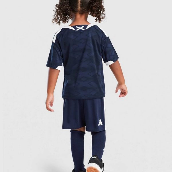 Back view of a child wearing a navy soccer jersey and shorts, navy socks, and black Adidas sneakers on a light background.