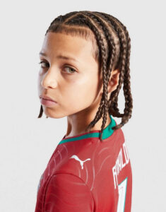 Young person with cornrow braids, wearing a red athletic jersey, looking over their shoulder.