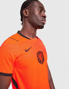 jd_789706_d | UAE SPORT STORE Side profile of a man wearing an orange soccer jersey with black trim and a lion crest on the chest.