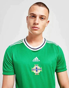Portrait of a young man wearing a green Adidas football jersey with a crest featuring a cross.