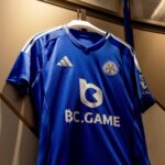 Blue Leicester City football club jersey on a white hanger in a closet, front view showing Adidas logo and club crest with BC.GAME sponsor.