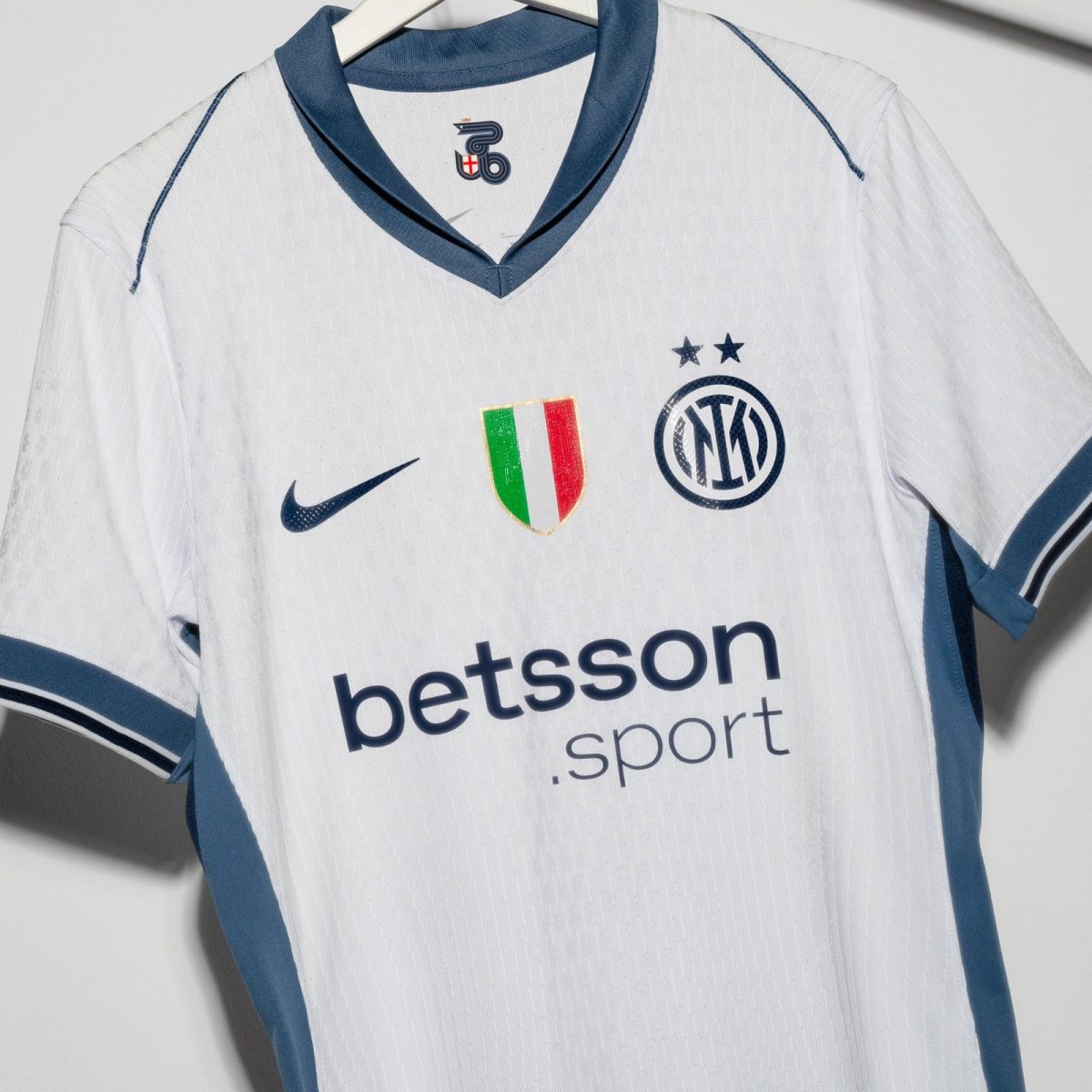 White Inter Milan football jersey on a hanger, blue collar and trim, featuring the Nike swoosh, Italian flag crest, Inter crest with two stars, and Betsson sponsor text.