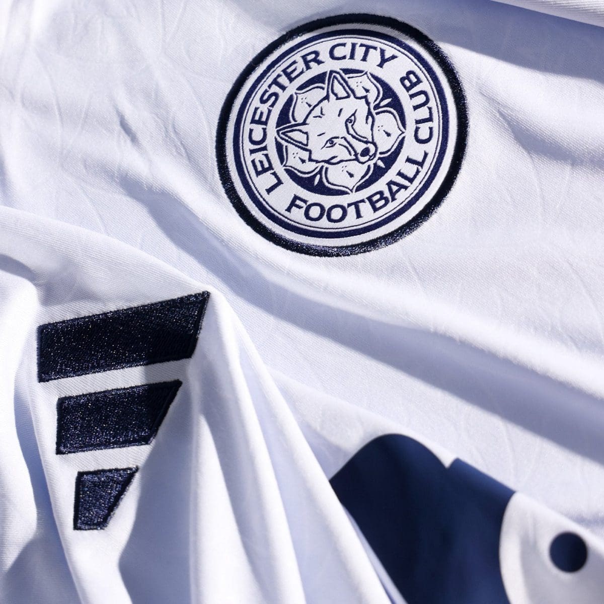 Circular Leicester City Football Club crest embroidered on a white jersey, featuring a fox head.
