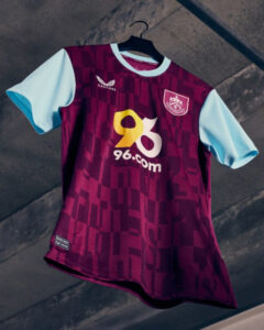 Maroon soccer jersey with light blue sleeves hanging on a hanger, displaying a yellow 96-com logo and team crest on the chest.