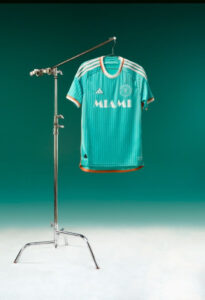 Turquoise Miami soccer jersey hanging on a metal stand in a studio background.