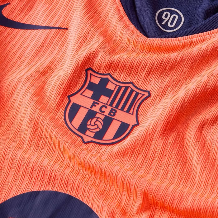 kg | UAE SPORT STORE Close-up of an orange FC Barcelona football jersey with crest and a 90 patch visible on the collar
