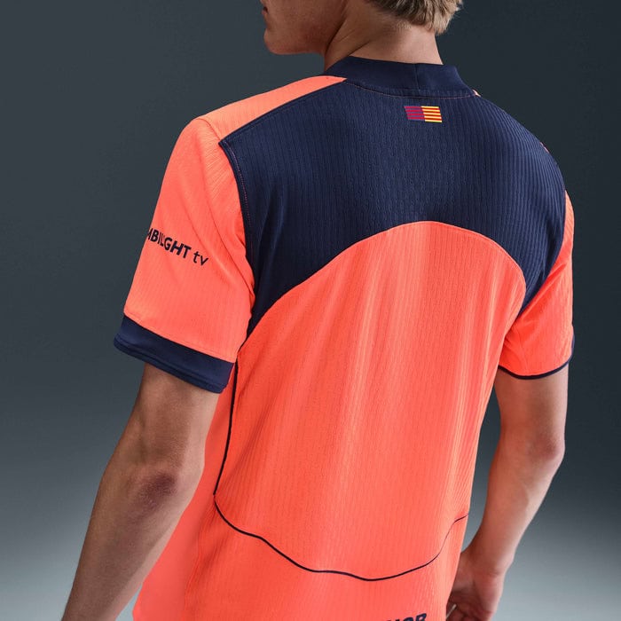 kh | UAE SPORT STORE Back view of a person wearing a neon orange and navy sports jersey with a small striped flag on the upper back and curved seam details.
