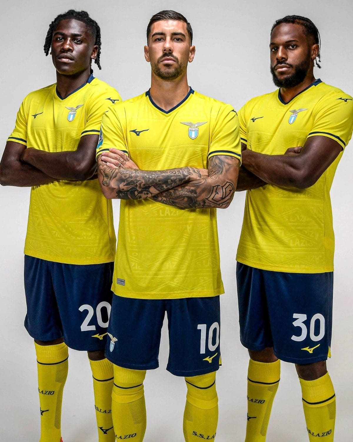 Three male soccer players in yellow Lazio jerseys pose with arms crossed