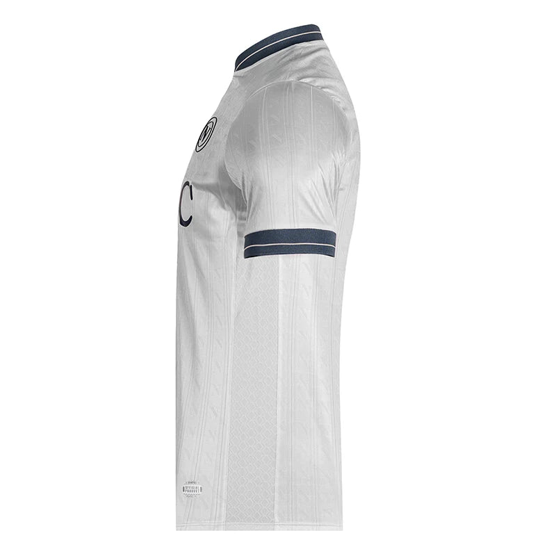 km_a49538bc-036a-47e4-ab9c-4a5d675fb73d | UAE SPORT STORE Side view of a white soccer jersey with dark blue collar and sleeve stripes, showing a crest and partial lettering on the chest.