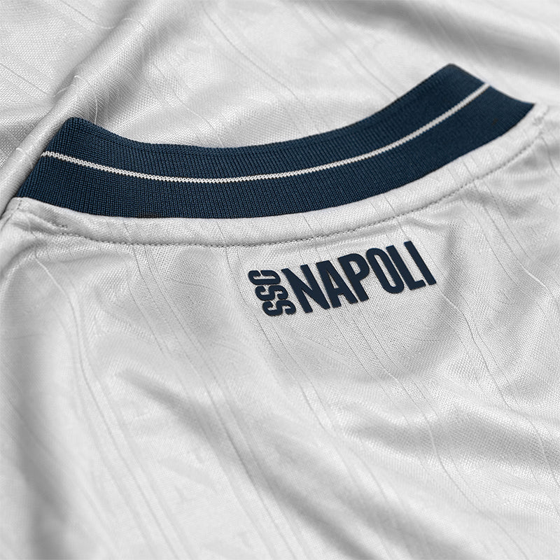 kn_d885a758-b40f-4825-b125-c6643a6d0be3 | UAE SPORT STORE Close-up of a white SSC Napoli football jersey with a navy collar and the 'SSC NAPOLI' name on the back.
