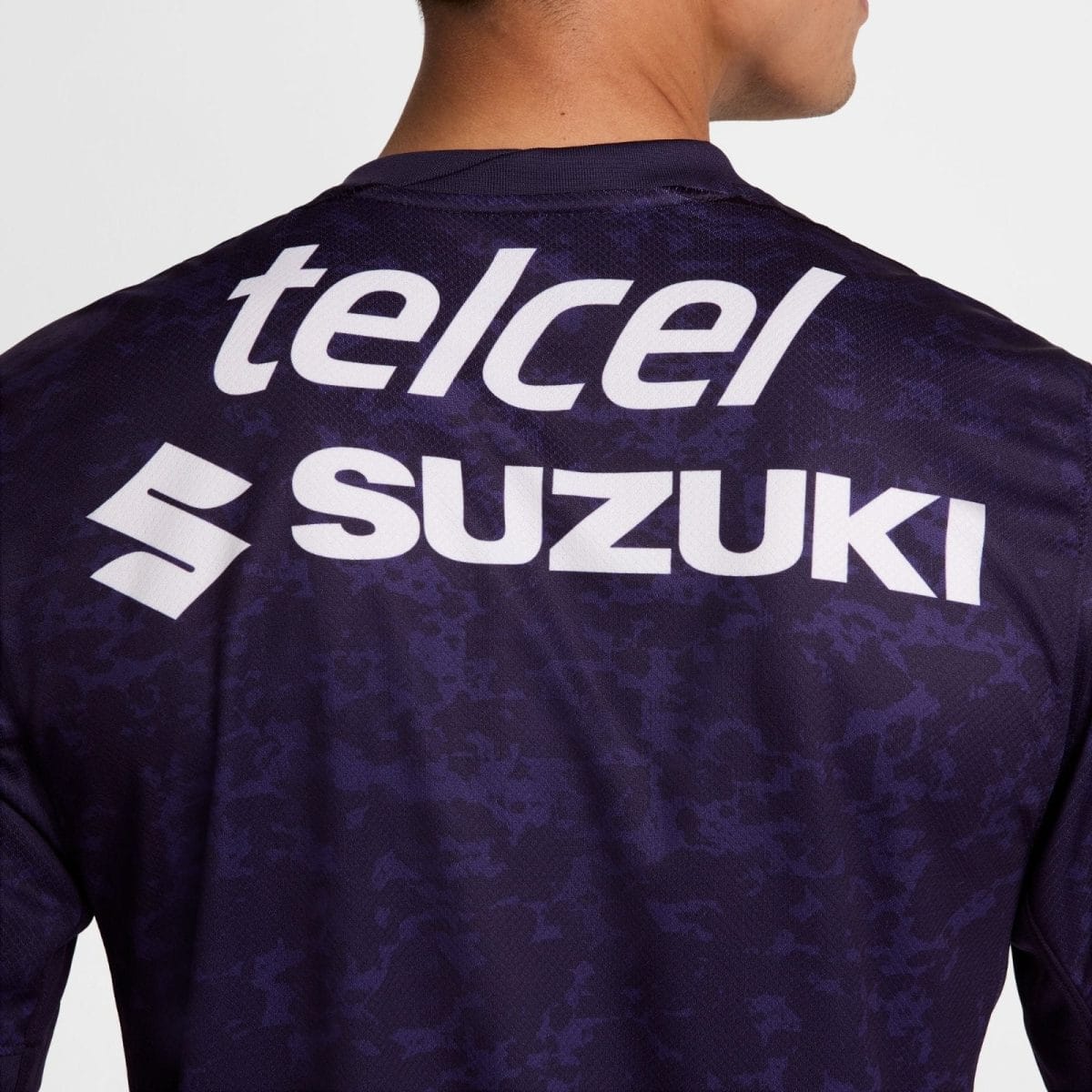 Back view of a person wearing a dark purple jersey with white Telcel and Suzuki logos.