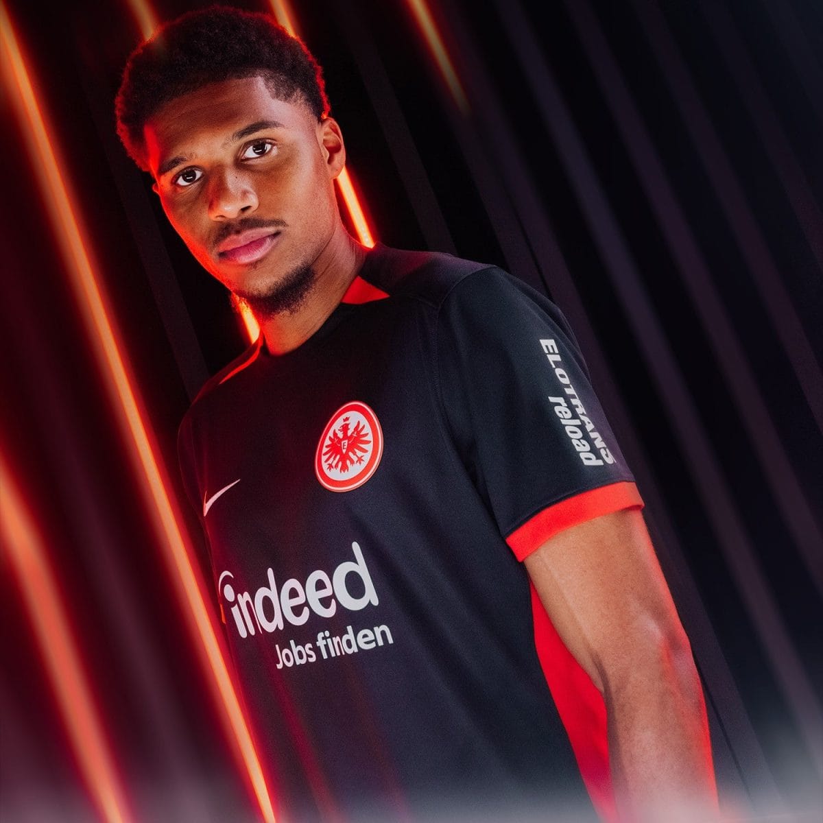 Portrait of a man wearing a black Eintracht Frankfurt jersey with red trim, set against red neon light lines in the background.