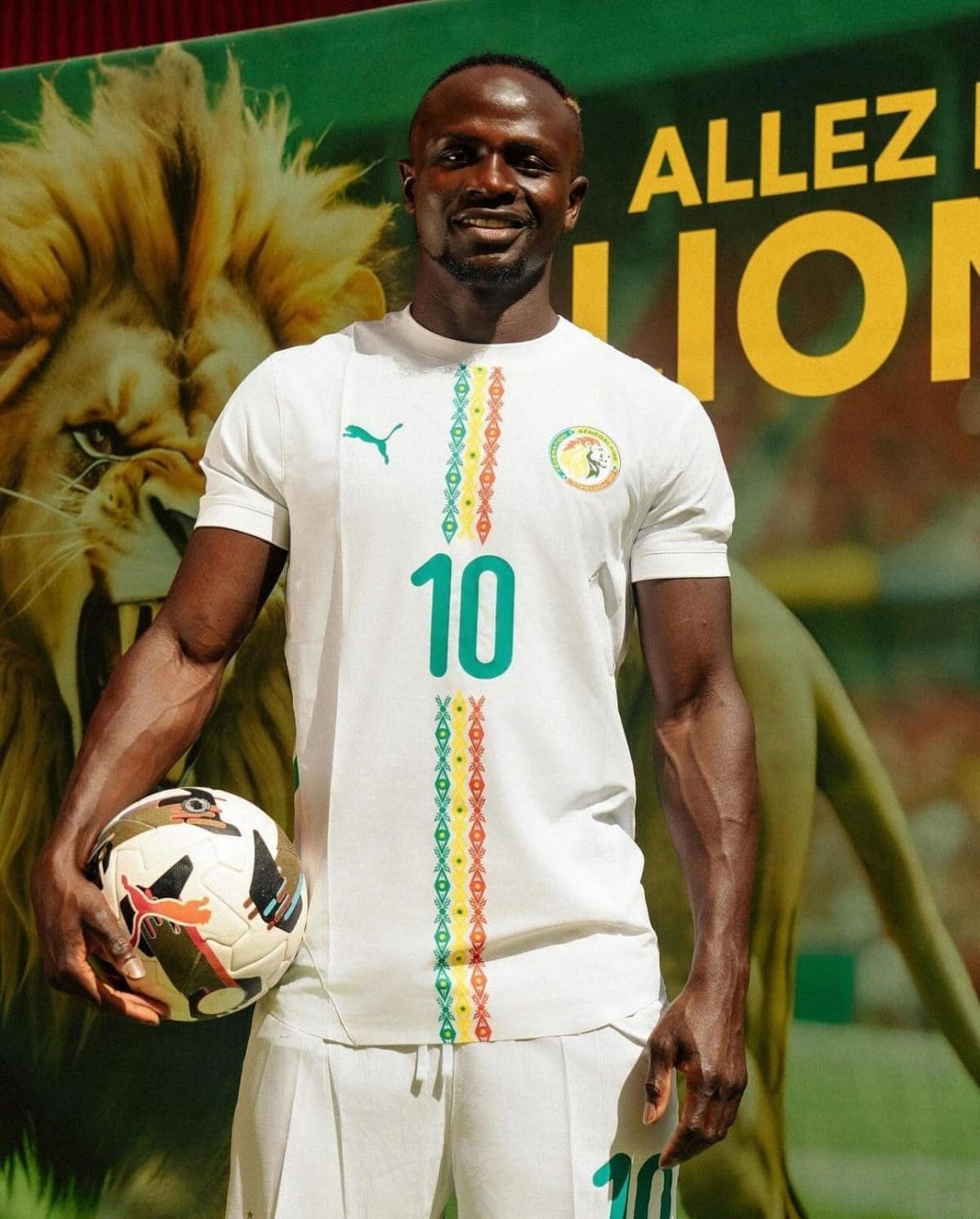 Male footballer in a white kit with the number 10, holding a soccer ball and smiling at the camera, colorful backdrop.